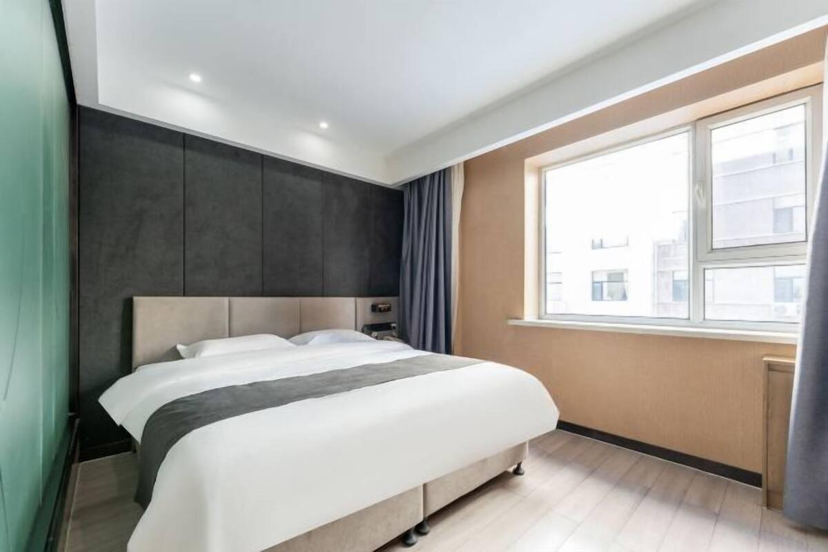 Ein modernes Hotelzimmer mit einem großen Bett, einem Fenster mit Vorhängen und Blick auf Gebäude.