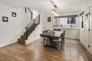 Ein Essbereich mit einem Holztisch und Stühlen, einer Treppe mit schwarzer Geländer und einem Fenster mit Jalousien.