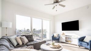 Ein modernes Wohnzimmer mit einem grauen Ecksofa, einem runden Couchtisch, einem blauen Sessel und einem weißen Fernseher an der Wand.