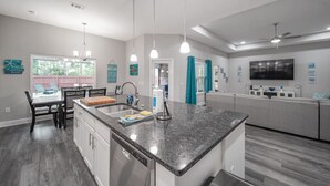 A modern kitchen with a central island, pendant lighting, and a dining area with a table and chairs. - Gorgeous 5 Bed/3 Bath, 10 Minutes To Navarre Beach (Navarre)