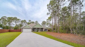 A single-story house with a front porch, a garage, and a driveway leading to the entrance. - Gorgeous 5 Bed/3 Bath, 10 Minutes To Navarre Beach (Navarre)