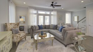A living room with a sectional sofa, a glass coffee table, a patterned armchair, and a staircase. - Stunning 2nd Row 3 Bedroom + Loft, 2.5 Bath Townhouse Myrtle Beach North End at Village at 74th (Myrtle Beach)