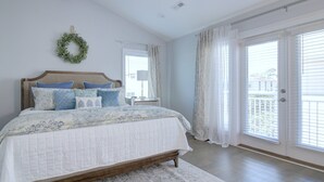 A bedroom with a bed, a nightstand, a lamp, a window with curtains, and a door with blinds. - Stunning 2nd Row 3 Bedroom + Loft, 2.5 Bath Townhouse Myrtle Beach North End at Village at 74th (Myrtle Beach)