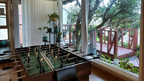 A room with a foosball table, large windows, and a view of a deck and trees outside. - Cozy Escape - Beach Community of Playa Del Rey (Los Angeles)