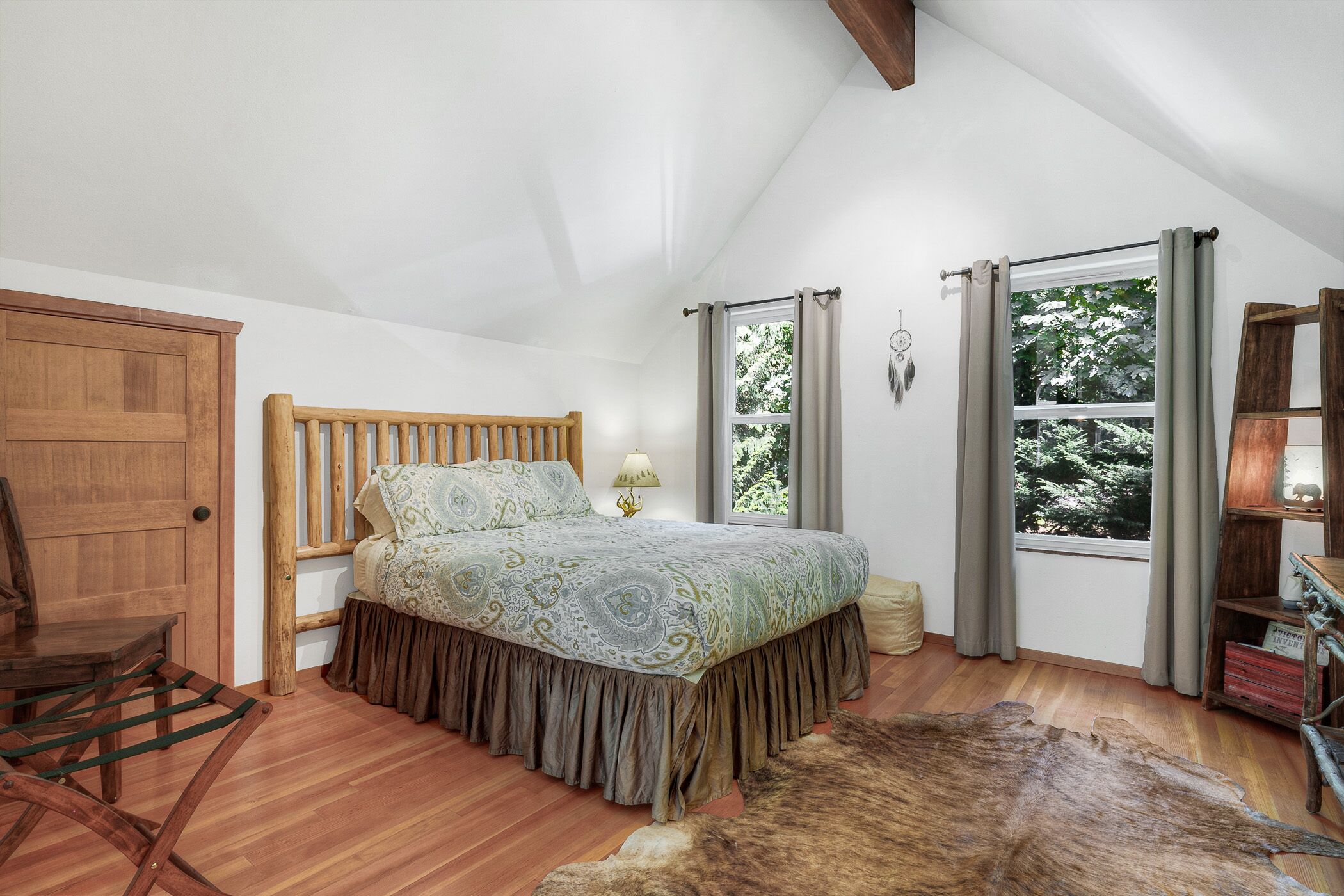A bedroom with a wooden bed, a wooden chair, a fur rug, and a window with curtains.