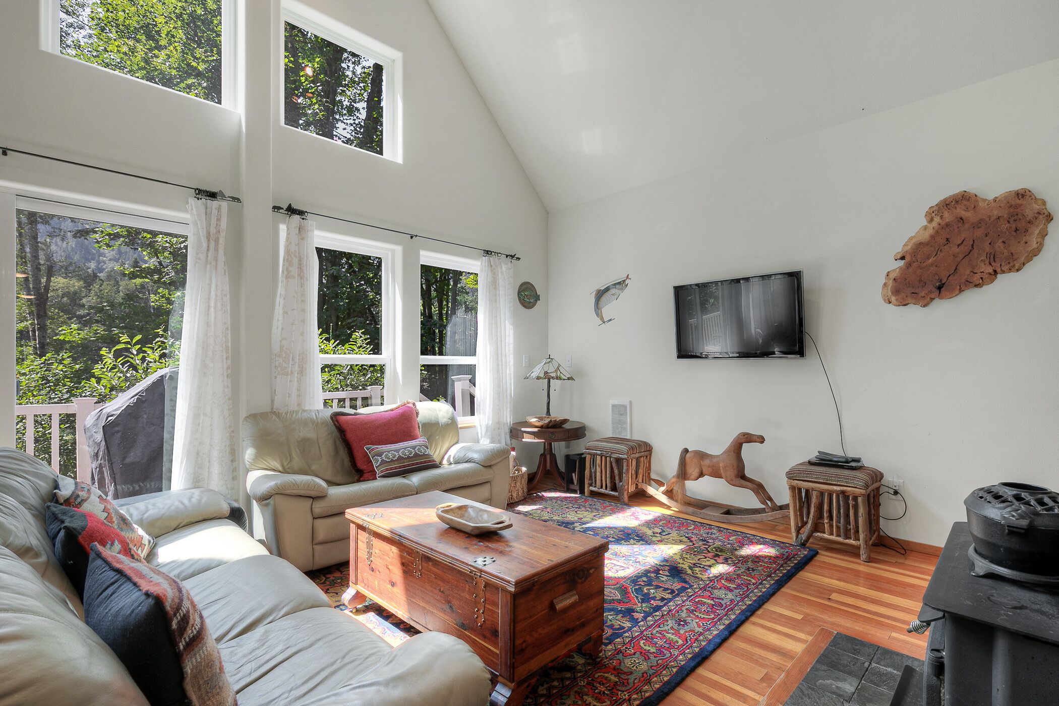 Ein geräumiges Wohnzimmer mit hoher Decke, großen Fenstern, einem Kamin und einem an der Wand befestigten Fernseher.
