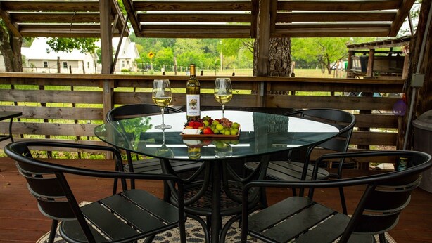 A round glass table with four black chairs, a bottle of white wine, and a fruit platter. - Windmill House | Hot Tub | Great Backyard (Fredericksburg)
