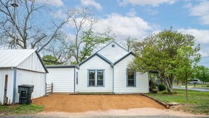 A single-story house with a gabled roof, a front porch, and a small attached shed. - Windmill House | Hot Tub | Great Backyard (Fredericksburg)