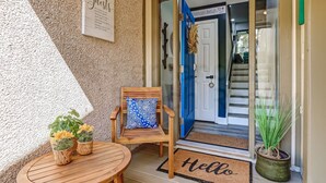 Una silla de madera con un cojín estampado y una mesita con plantas en macetas frente a una puerta.