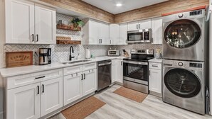 Cocina moderna con armarios blancos, horno empotrado, microondas y lavadora de acero inoxidable.