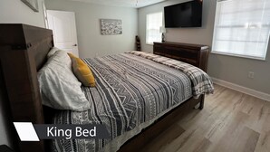 Et soveværelse med en king-size seng, loftventilator, fladskærms-TV og et vindue med persienner.