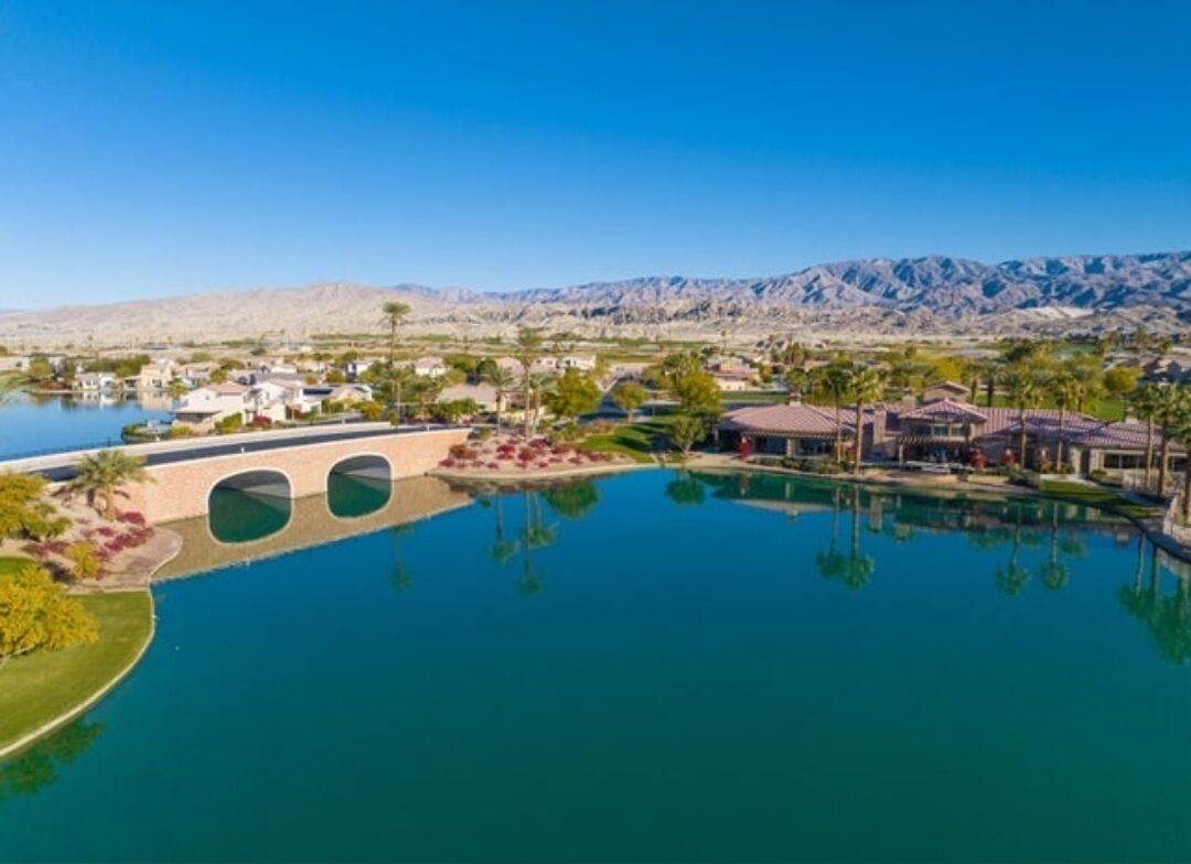 A resort with a large swimming pool, a bridge, and a mountainous backdrop.
