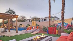 Patio trasero con un brasero, asientos exteriores, una piscina y una pérgola.