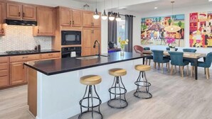 Una cocina moderna con armarios de madera, encimera negra y una isla central con taburetes.