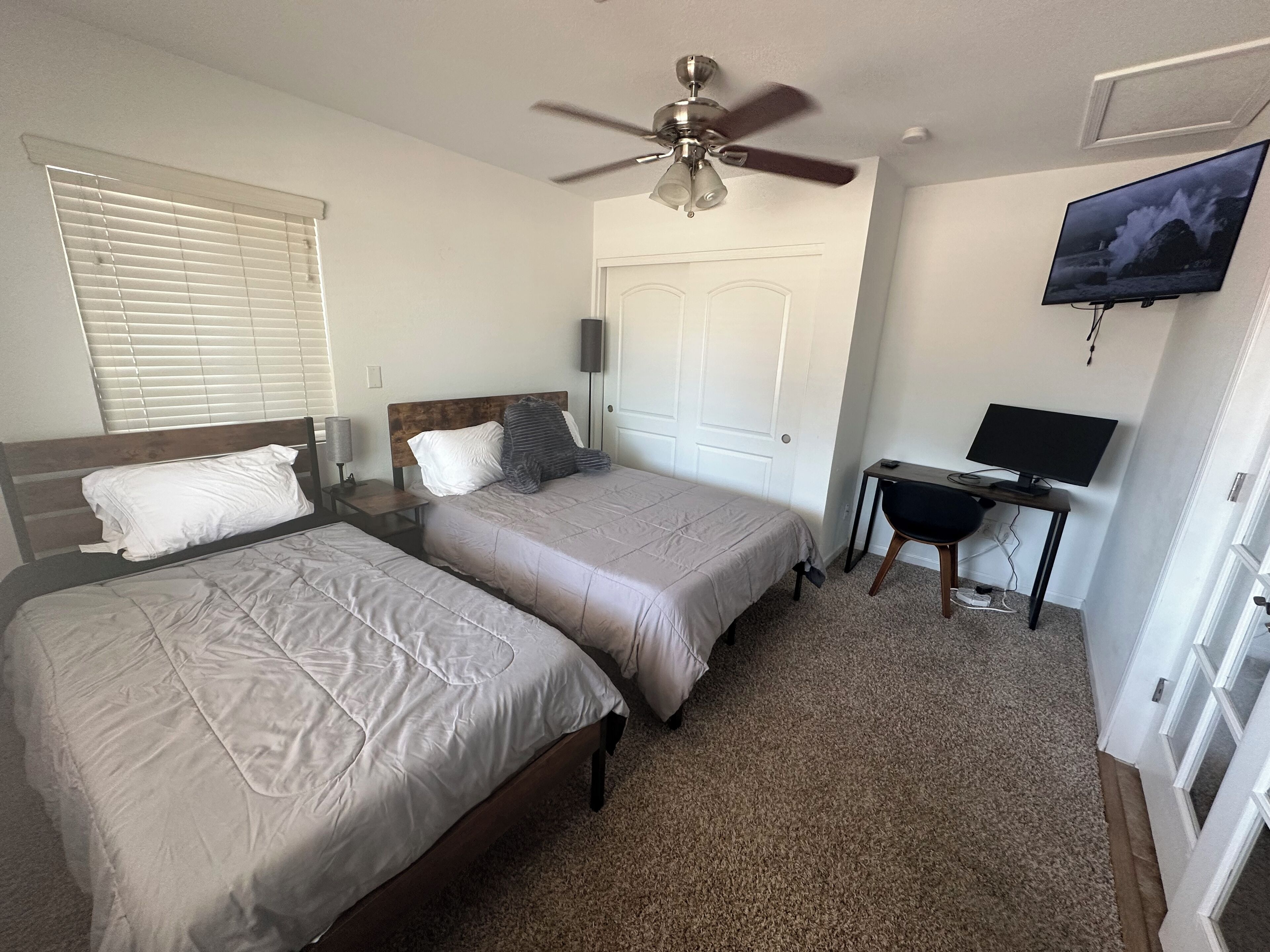 A bedroom with two beds, a ceiling fan, a TV, and a desk.