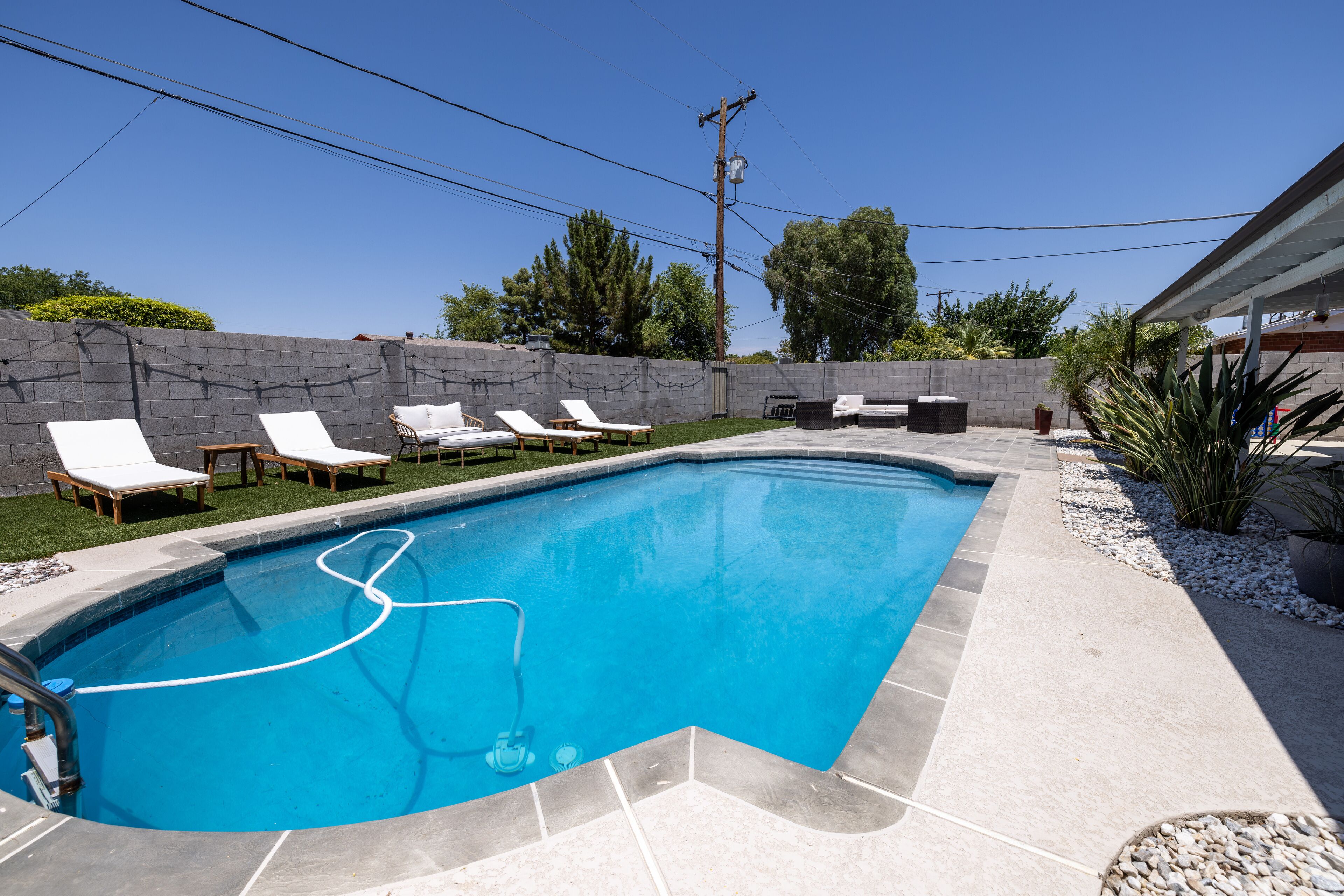 A rectangular swimming pool with a tiled deck, surrounded by a low stone wall, and equipped with lounge chairs and a barbecue area.