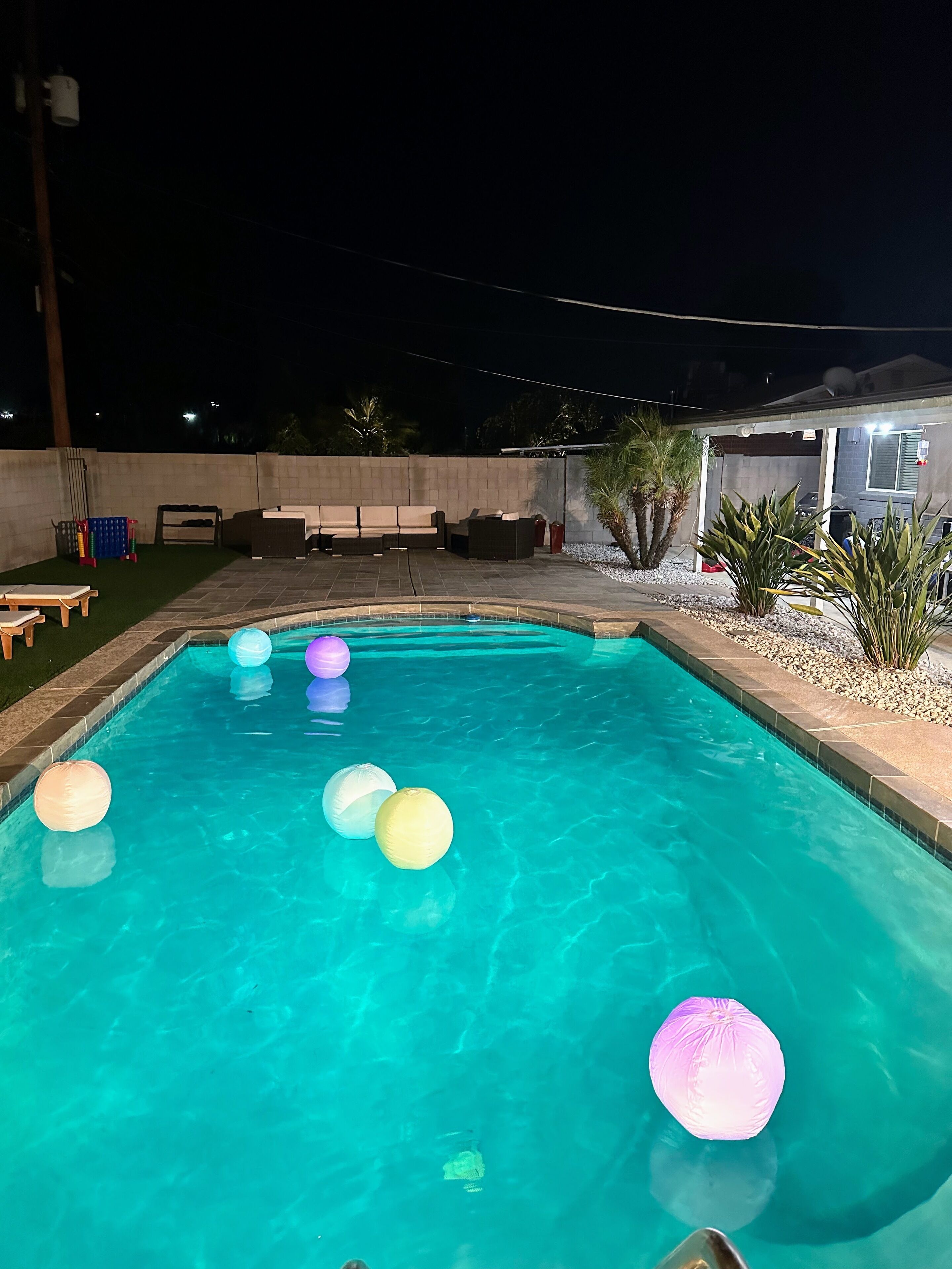 A swimming pool with floating lanterns, surrounded by a patio area with seating and a small building.