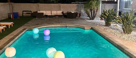 A swimming pool with floating lanterns, surrounded by a patio area with seating and a small building.