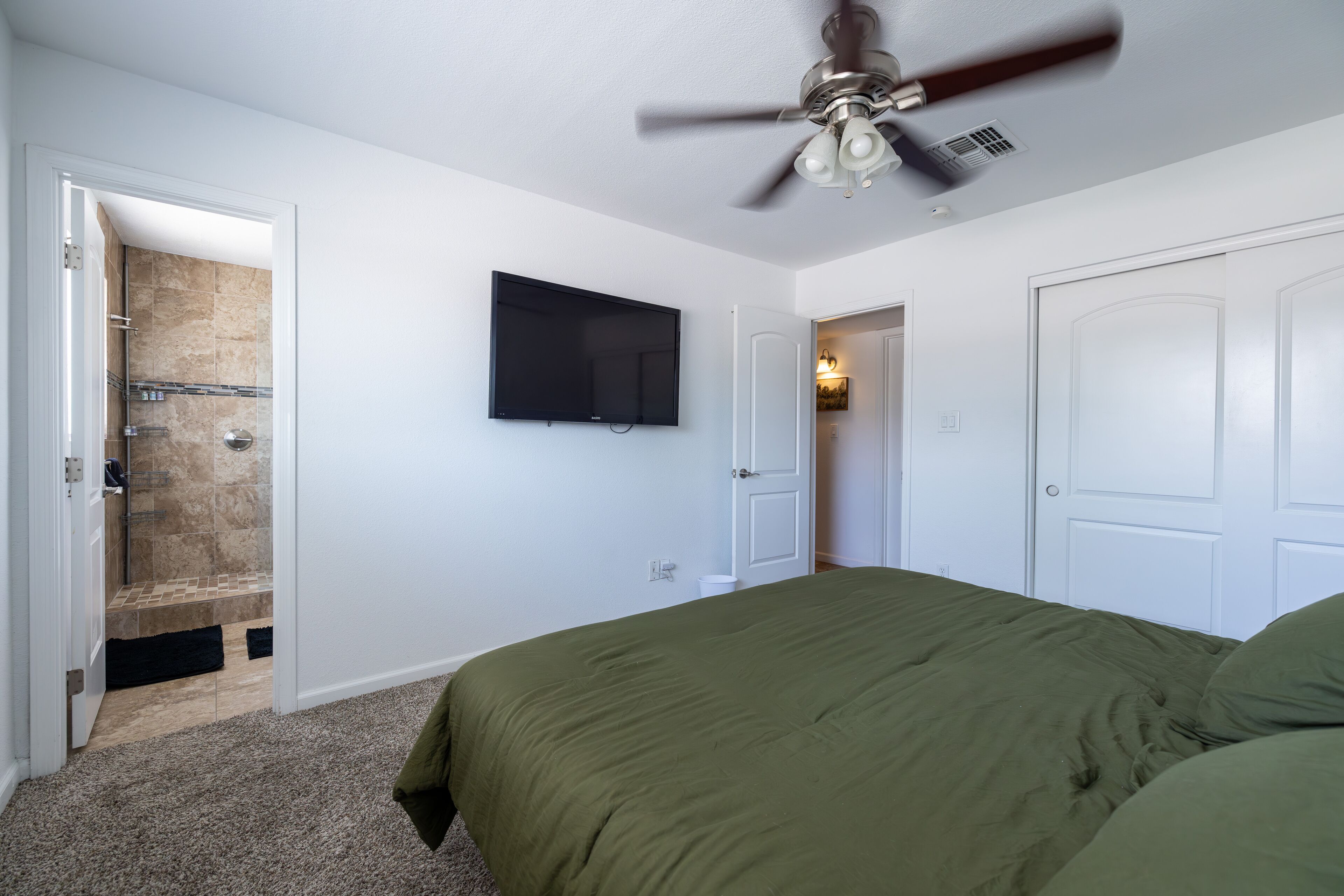 A bedroom with a green bedspread, a ceiling fan, a mounted TV, and a walk-in closet.
