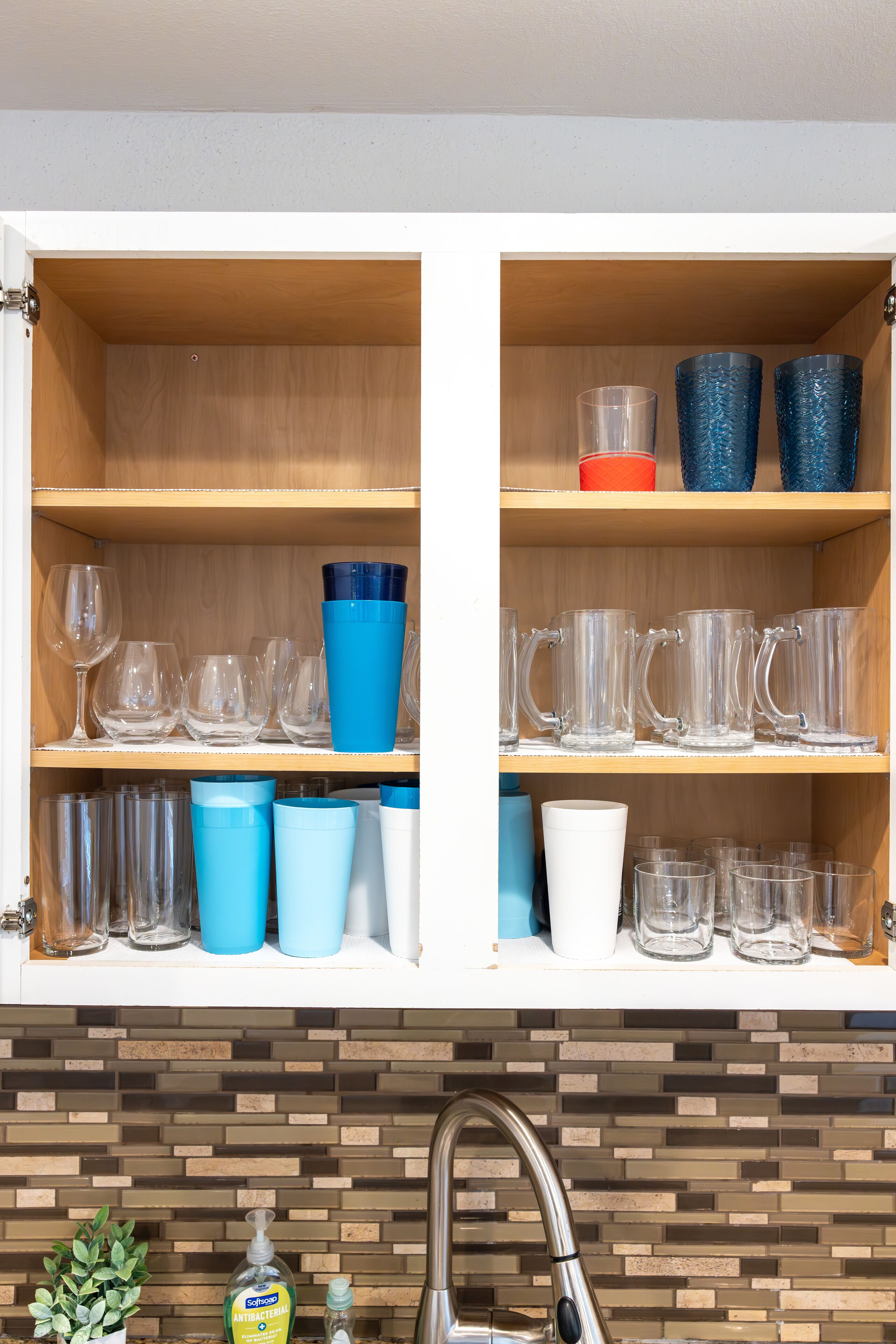 A kitchen with wooden shelves holding various glassware and a tiled backsplash.