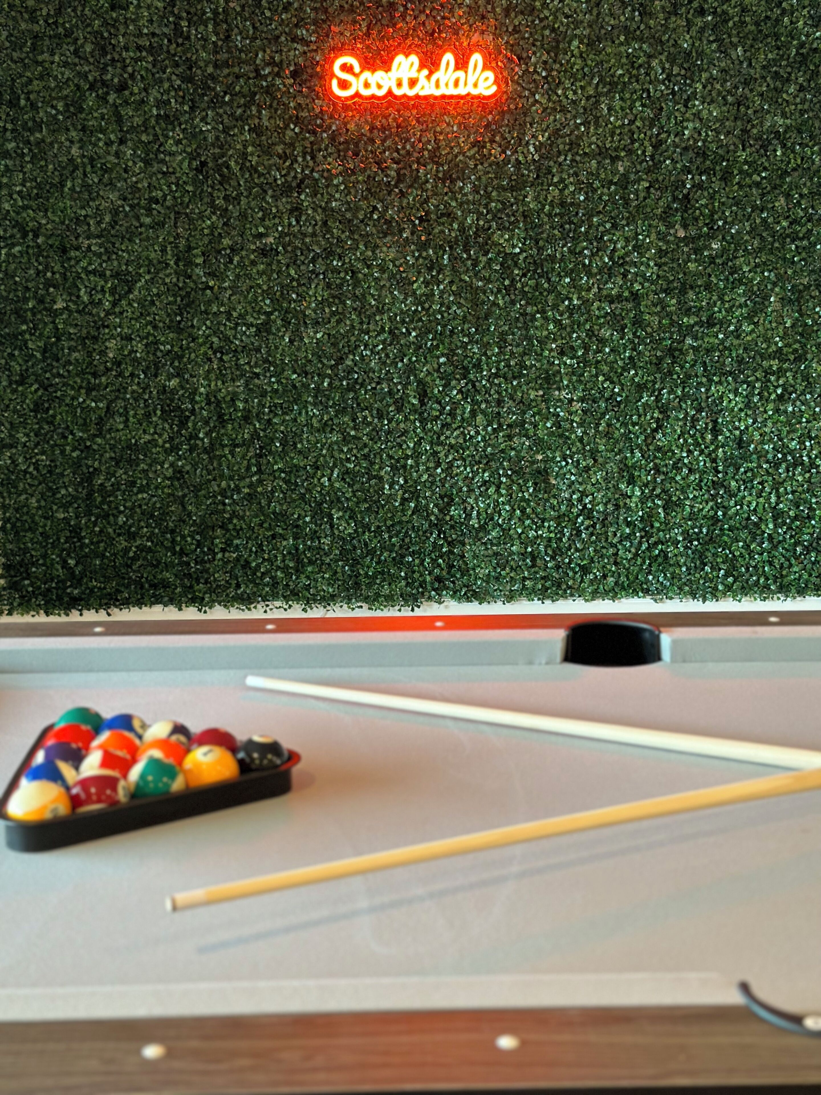 A pool table with balls and a cue stick, a neon sign reading "Scottsdale", and a green textured wall.