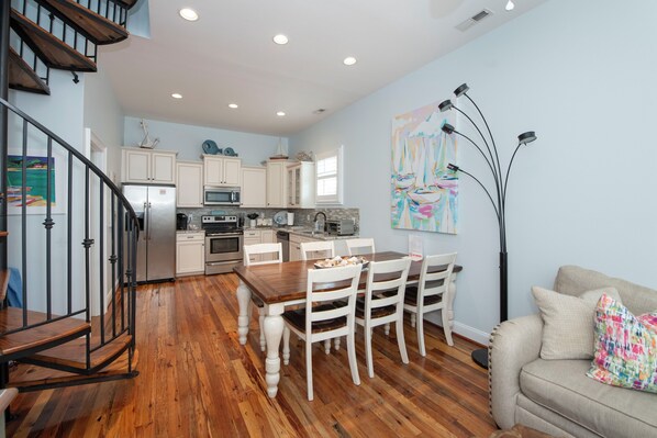 A modern kitchen with white cabinets, stainless steel appliances, and a dining area with a wooden table and white chairs. - 5 Star Reviews! Luxury Home, Pool, Steps from Ocean,Sleeps 7, Shops,Restaurants (Atlantic Beach)