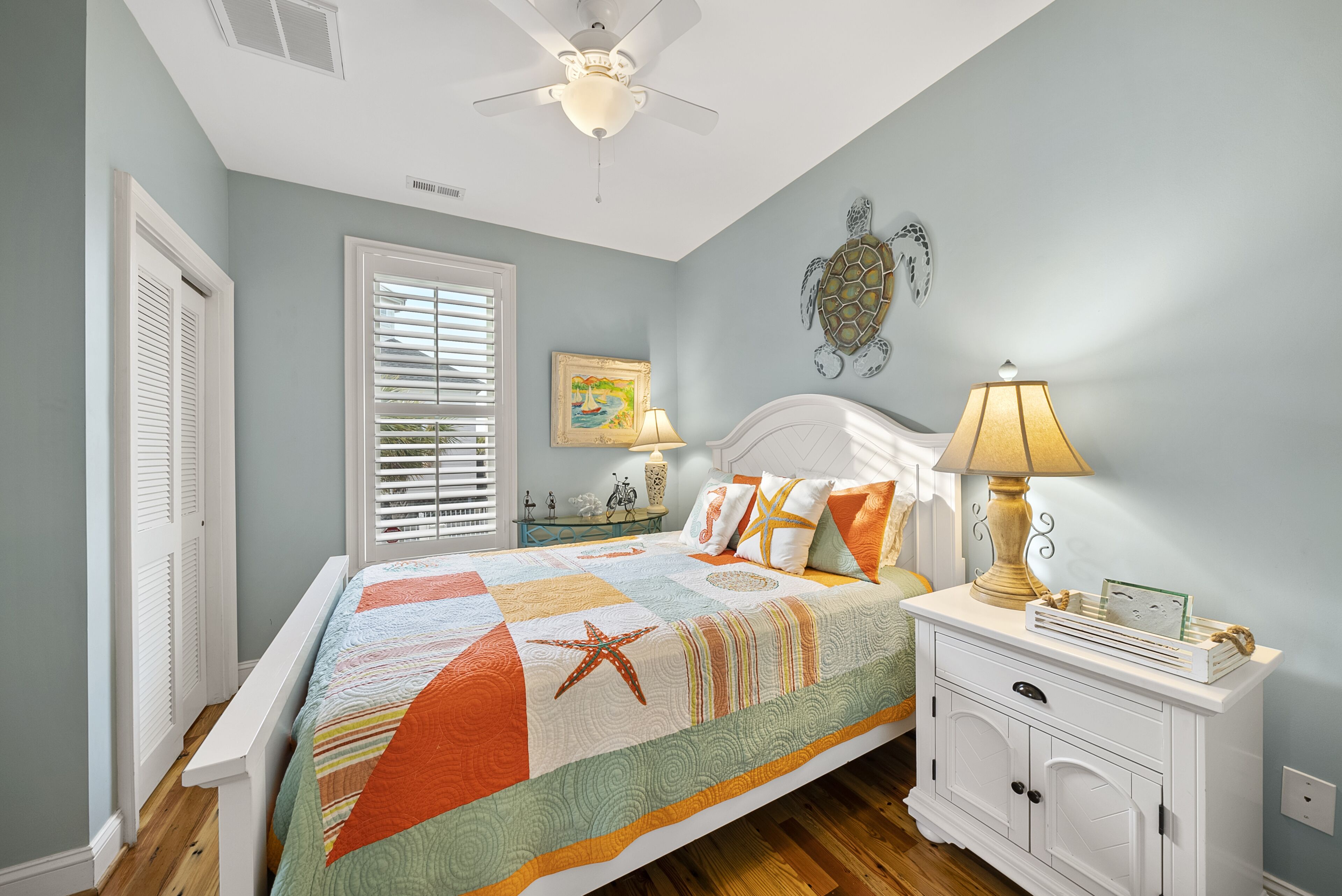 A bedroom with a bed, a nightstand, a ceiling fan, a window with blinds, and a wall decoration.