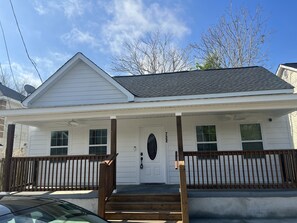 Stylish home with a front porch, wooden railing, and bench, set amidst a yard with a wooden fence.