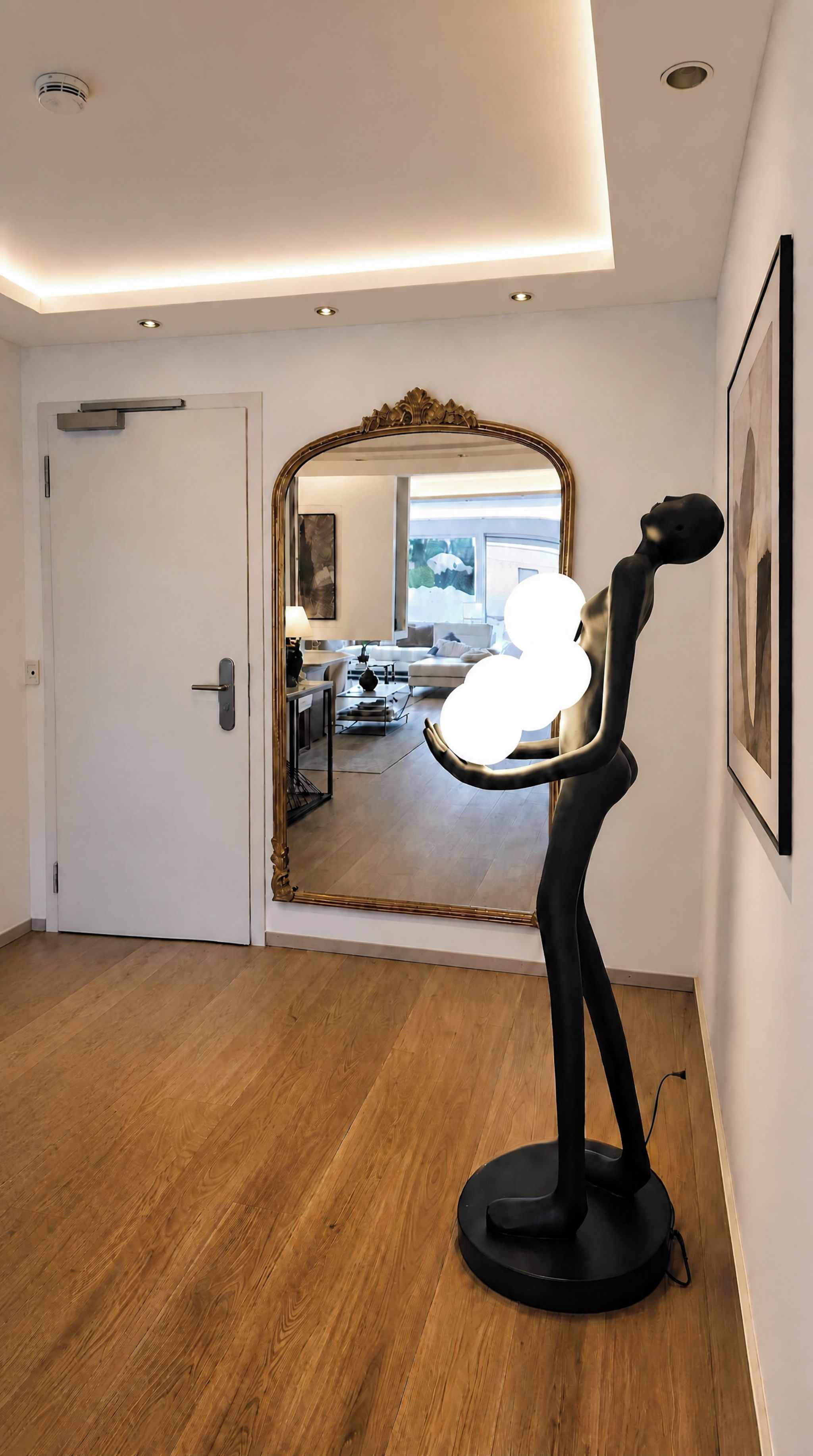 Een modern interieur met een houten vloer, een grote spiegel en een sculptuur.