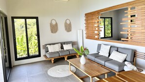 A modern living room with a grey sofa, wooden coffee table, and a large window with a view of greenery. - Fantastic Ocean View Villa (Dominical)