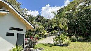 A modern house with a white exterior, a paved driveway, and a well-maintained garden with various plants and a small bridge. - Fantastic Ocean View Villa (Dominical)