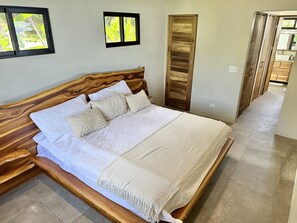 Une chambre à coucher avec un cadre de lit en bois, une grande couvre-lit et une vue sur la cuisine par une porte ouverte.