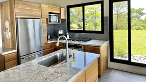 A modern kitchen with a stainless steel refrigerator, a microwave, a gas stove, and a large window offering a view of a green landscape. - Fantastic Ocean View Villa (Dominical)