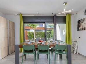 A modern dining area with a wooden table, green chairs, and a view of a garden through large windows.