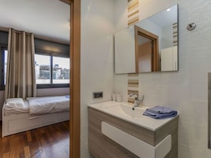Une chambre d’hôtel moderne, équipée d’un lit, d’une salle de bain avec un lavabo et un miroir, et d’une fenêtre avec des rideaux.