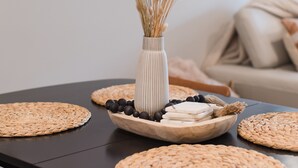 A dining table with woven placemats, a bowl of olives, a vase with dried wheat stalks, and a white vase with a striped pattern. - Experiencing Edmonds, In the Heart of it All! (Edmonds)