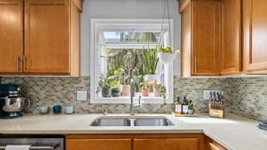 A kitchen with wooden cabinets, a brick backsplash, a window with plants, and a stainless steel sink. - Experiencing Edmonds, In the Heart of it All! (Edmonds)