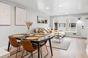 A modern living room with a dining area, featuring a sofa, coffee table, and a dining table with chairs.