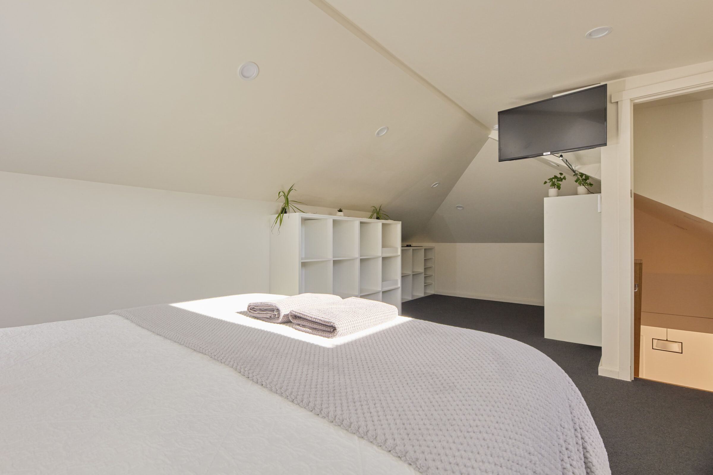 A bedroom with a bed, a TV mounted on the wall, and a staircase leading to an upper level.