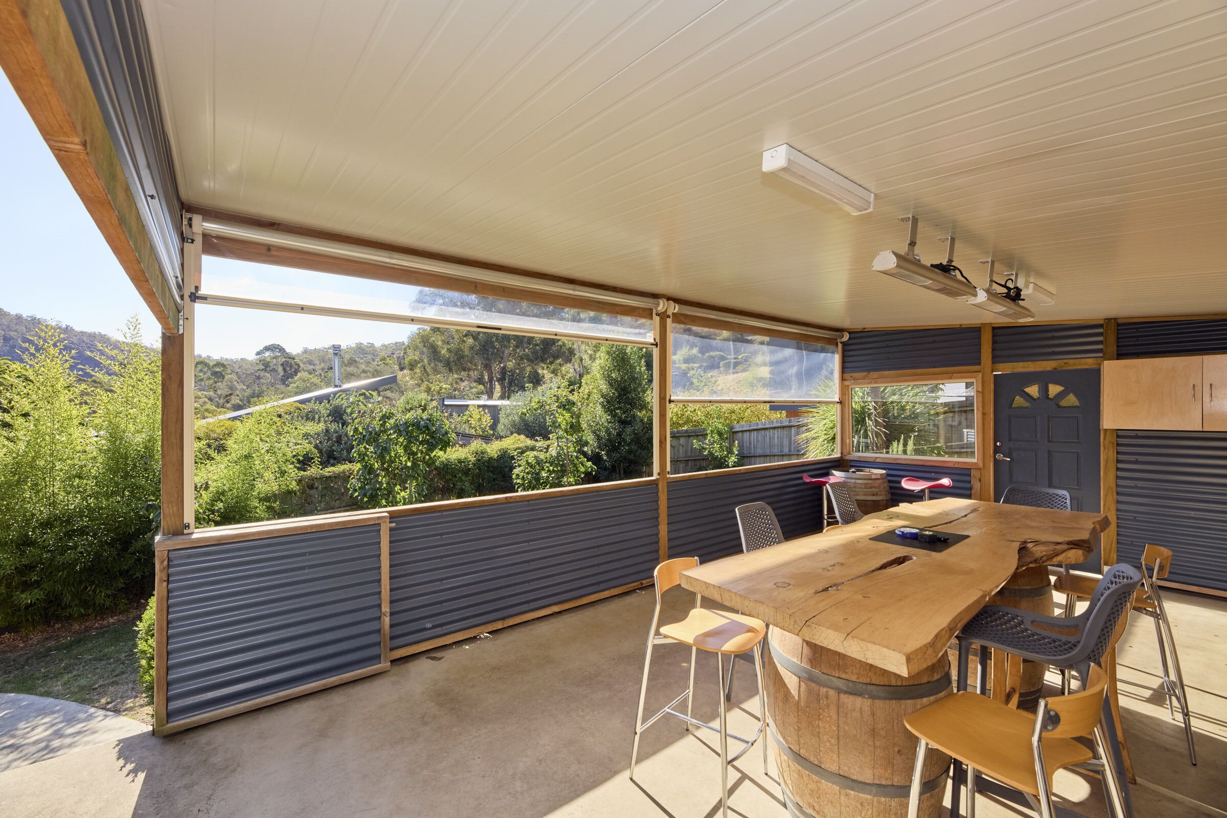 An outdoor dining area with a wooden table and chairs, a view of the surrounding greenery, and a ceiling fan.