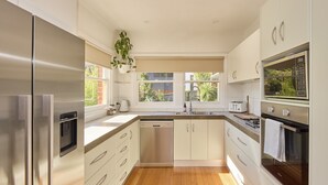 A modern kitchen with stainless steel appliances, white cabinetry, and a wooden floor. - Basin Road Guesthouse | Walk to Cataract Gorge & CBD (West Launceston)