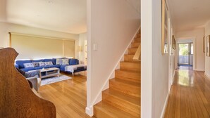 A spacious living room with a blue sofa, wooden flooring, and a staircase leading to another level. - Basin Road Guesthouse | Walk to Cataract Gorge & CBD (West Launceston)