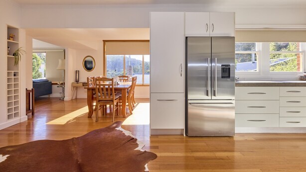 A modern kitchen with a stainless steel refrigerator, wooden dining table, and white cabinetry. - Basin Road Guesthouse | Walk to Cataract Gorge & CBD (West Launceston)