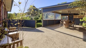 An outdoor patio area with a table and chairs, a wooden bench, and a view of the surrounding greenery and hills. - Basin Road Guesthouse | Walk to Cataract Gorge & CBD (West Launceston)