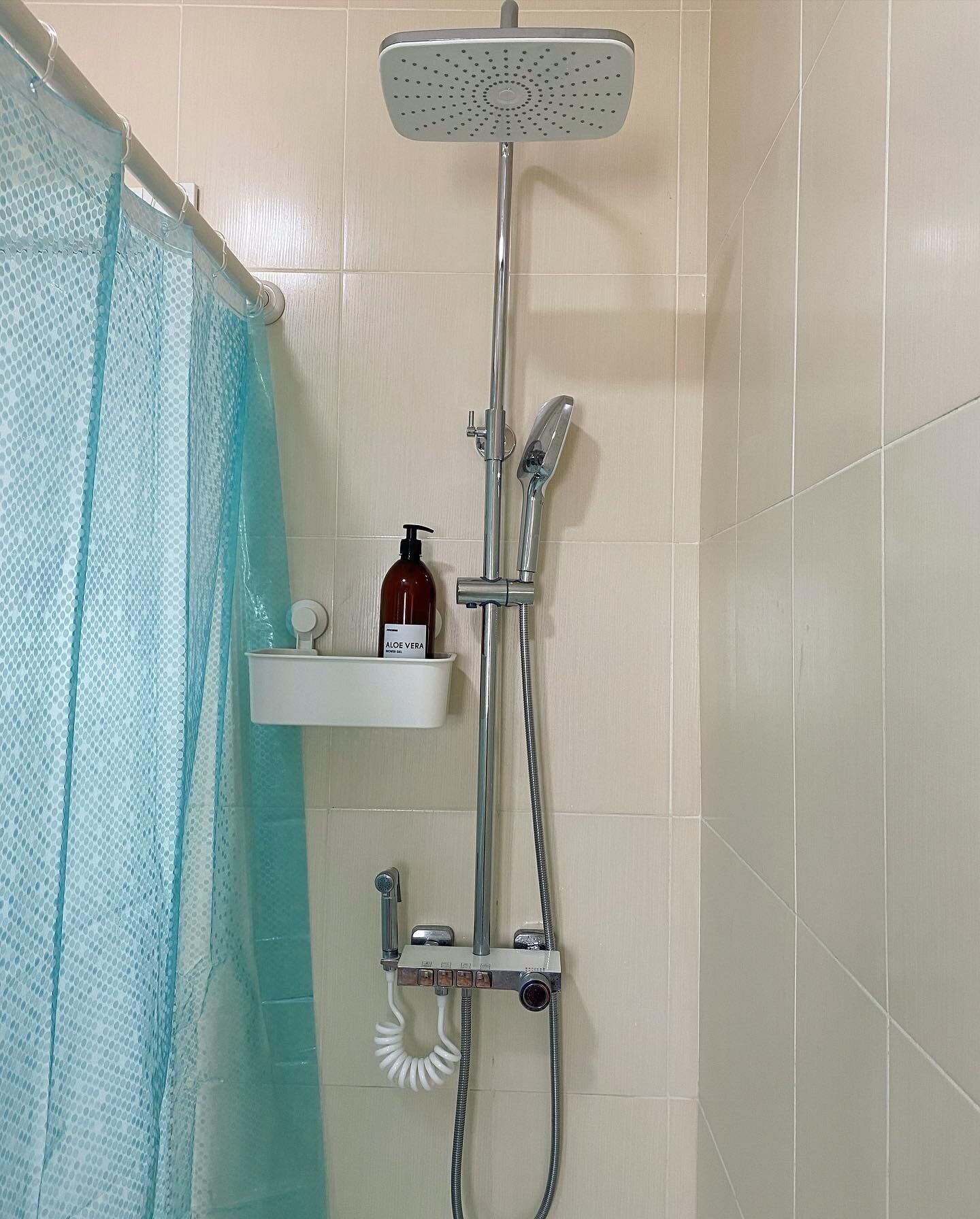 A shower with a handheld showerhead, a wall-mounted faucet, and a handheld shower hose. There is a soap dispenser on a shelf below the shower.