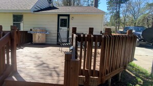 A wooden deck with a grill and a table, a house with a door, and a vehicle parked outside. - cozy 2 bedroom close to trails and boat launch three minutes (Richfield Township)