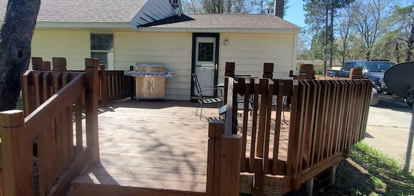 A wooden deck with a grill and a table, a house with a door, and a vehicle parked outside. - cozy 2 bedroom close to trails and boat launch three minutes (Richfield Township)