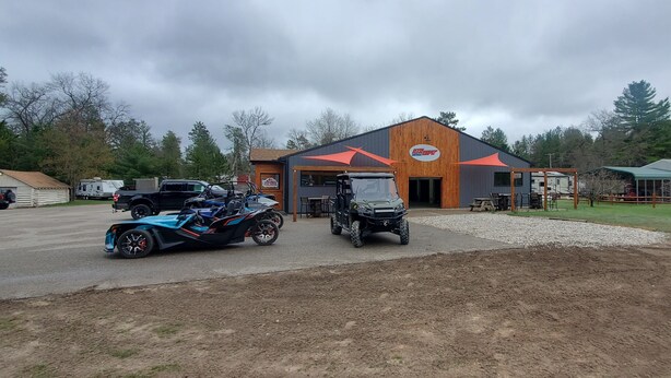 A building with a prominent logo, a gravel driveway, and several vehicles parked in front. - cozy 2 bedroom close to trails and boat launch three minutes (Richfield Township)