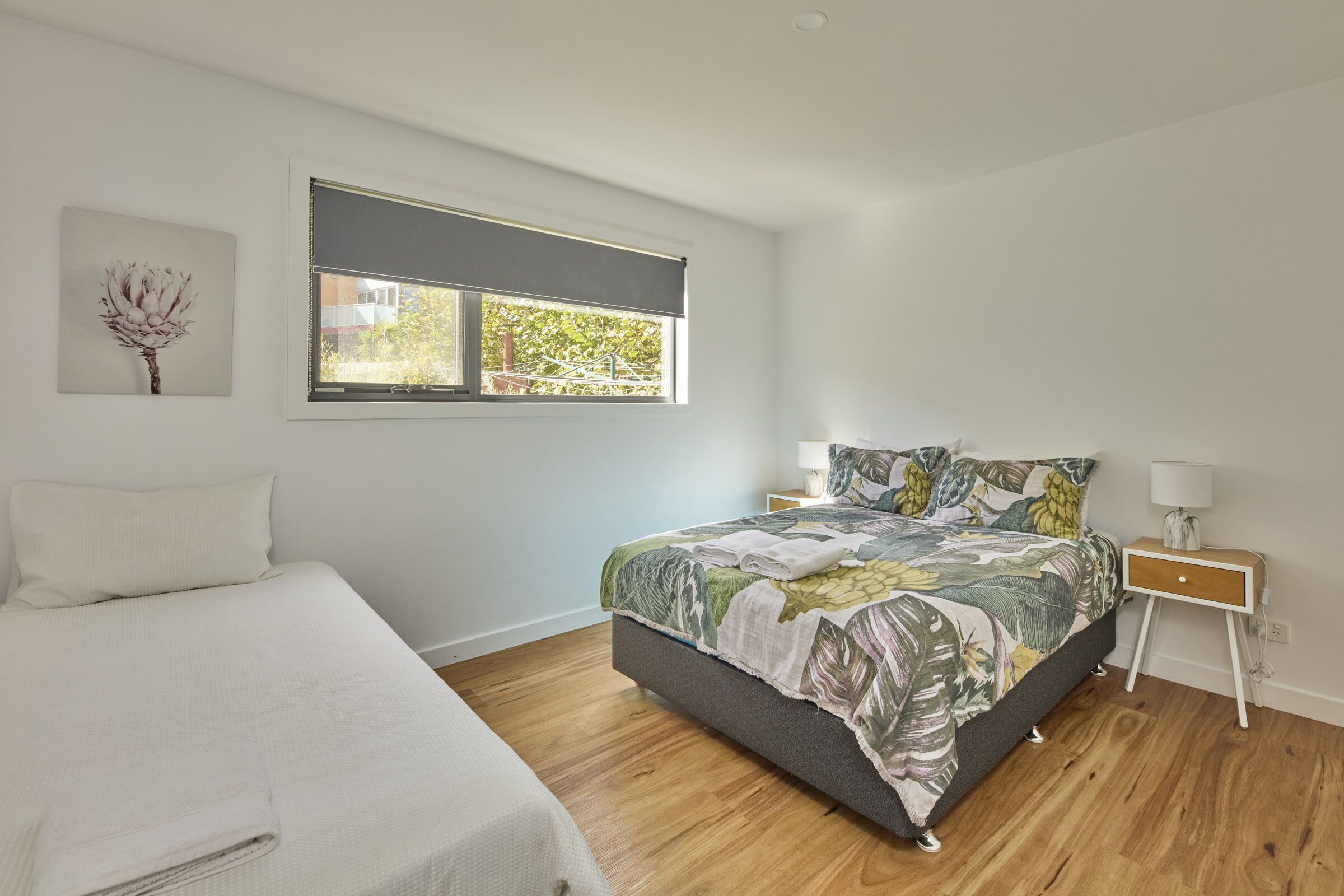 A bedroom with a bed, a nightstand, a window with a view, and a wall-mounted artwork.