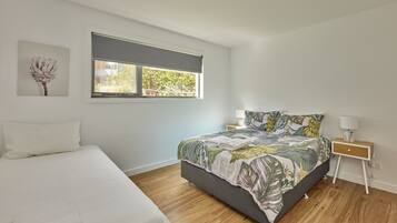 A bedroom with a bed, a nightstand, a window with a view, and a wall-mounted artwork.